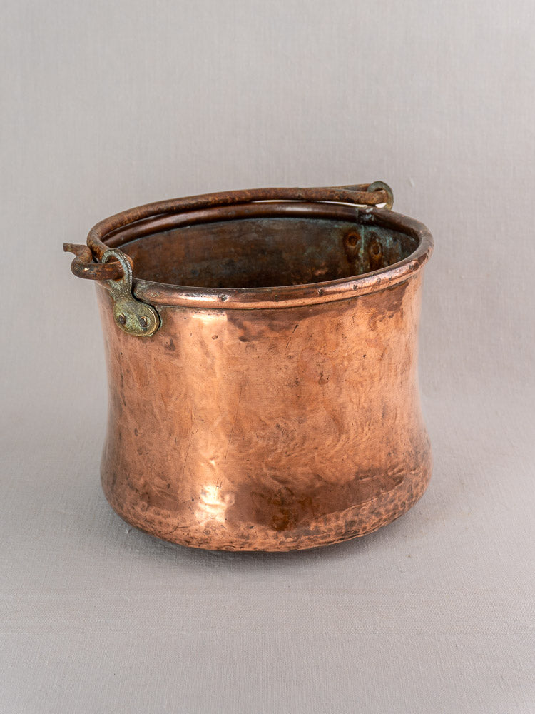 Antique French copper cauldron with hammered finish and iron bail handle, set against a light gray background.