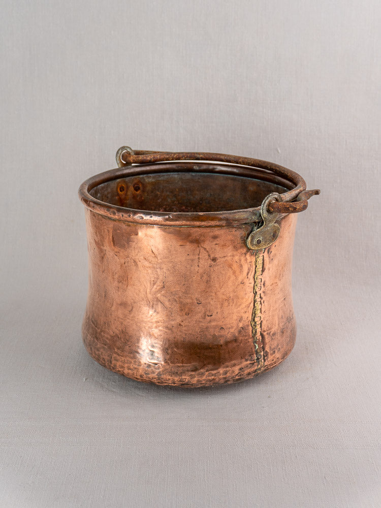 Antique French copper cauldron with hand-hammered finish and iron bail handle on a light gray background.