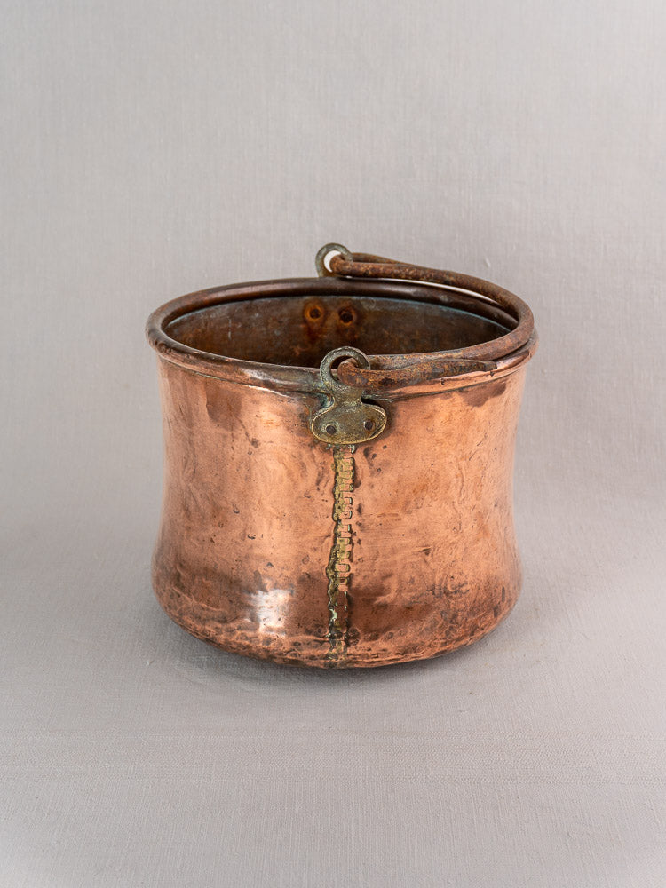 Antique French copper cauldron with hand-hammered round body, wide opening, green patina, and iron bail handle.