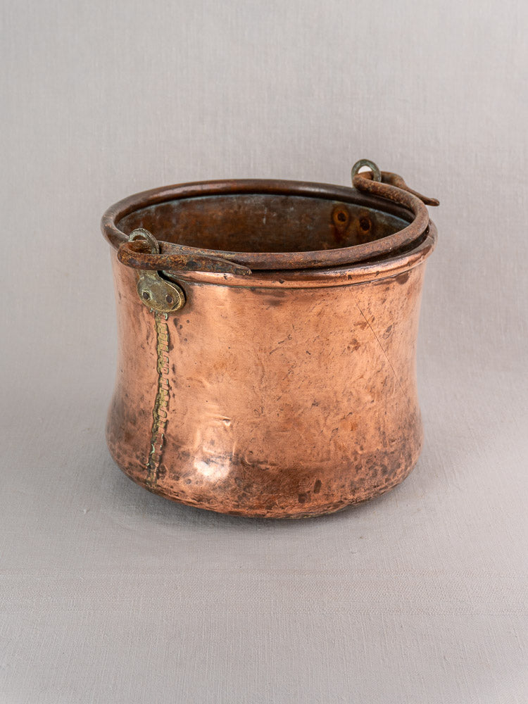 Antique French copper cauldron with hand-hammered finish, flared rim, visible seam, and iron bail handle.