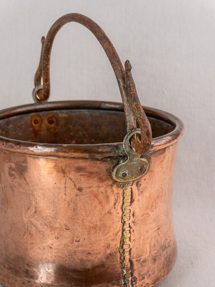 Antique French copper cauldron with hand-hammered details, iron bail handle, and visible repairs on a neutral background.