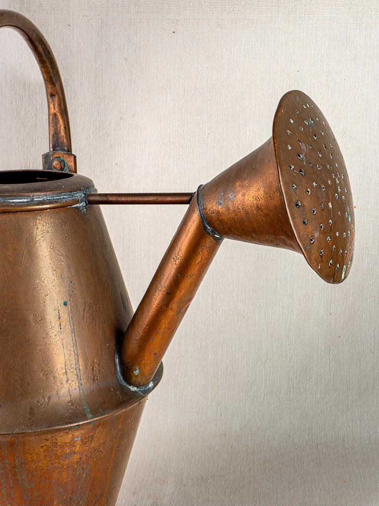 Vintage French copper watering can by Jean Goardère, Villedieu MOF, with perforated spout and handle on beige background.