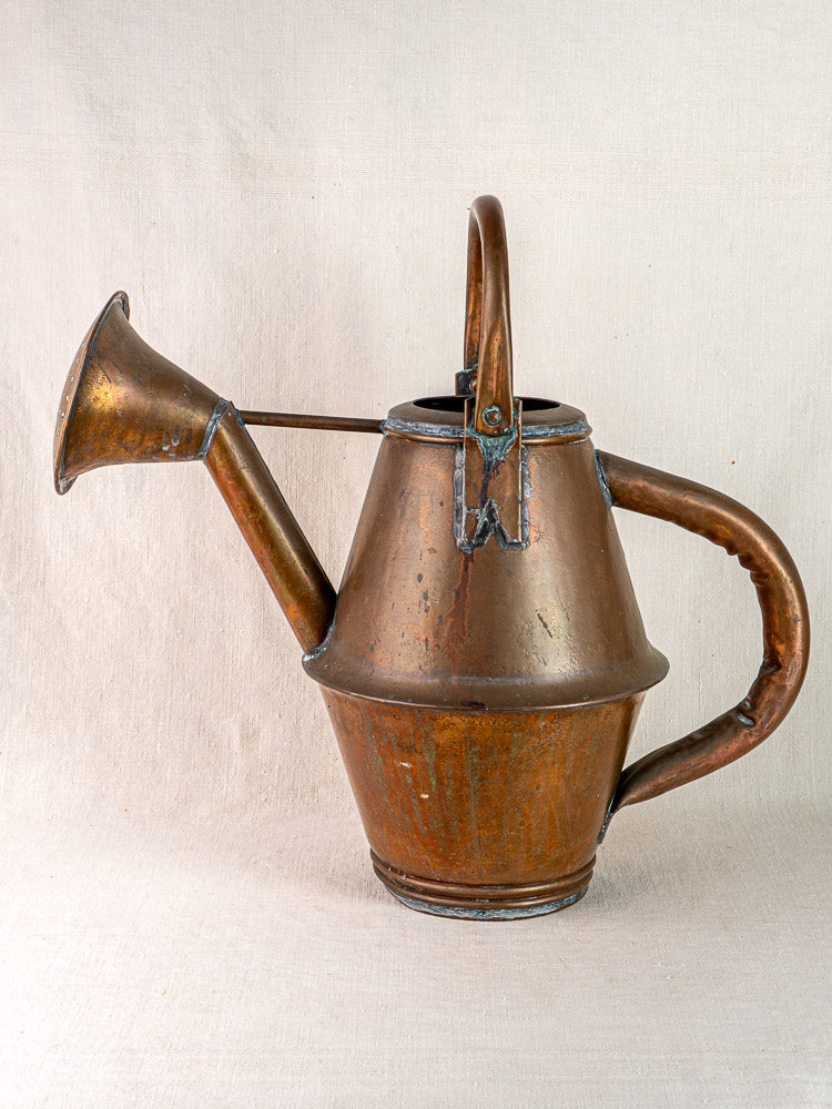 Vintage French copper watering can by Jean Goardère with curved handle and flared spout, on light fabric background.
