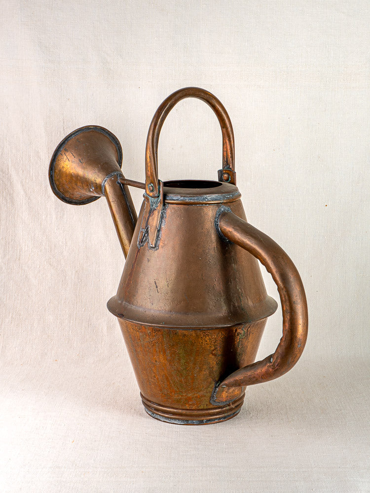 Vintage French copper watering can by Jean Goardère, Villedieu MOF, on neutral fabric background.