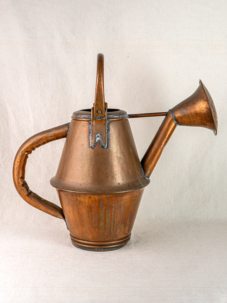 Vintage French copper watering can by Jean Goardère with large handle and wide spout, on light fabric.