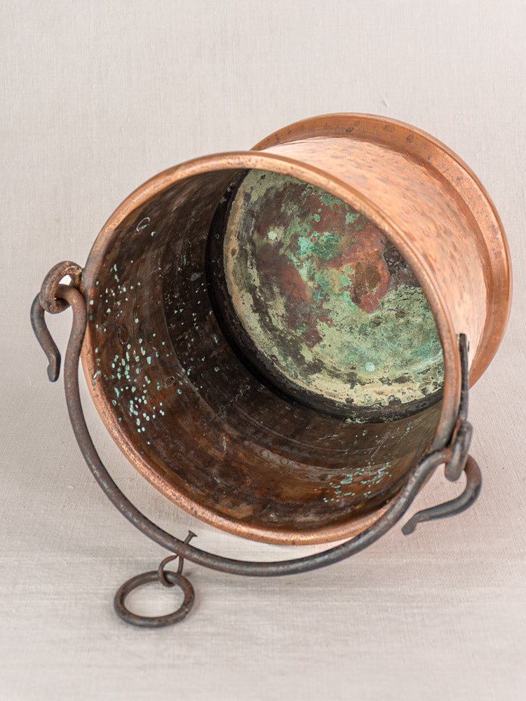 Antique French copper hanging bucket with hammered finish, metal handle, and green patina on a neutral background.