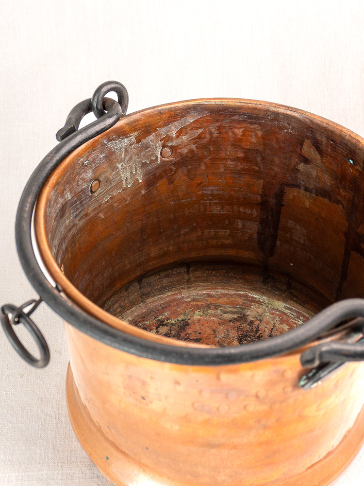 Pair of 19th-century French copper hanging buckets with hammered texture and dark handles on light fabric background.