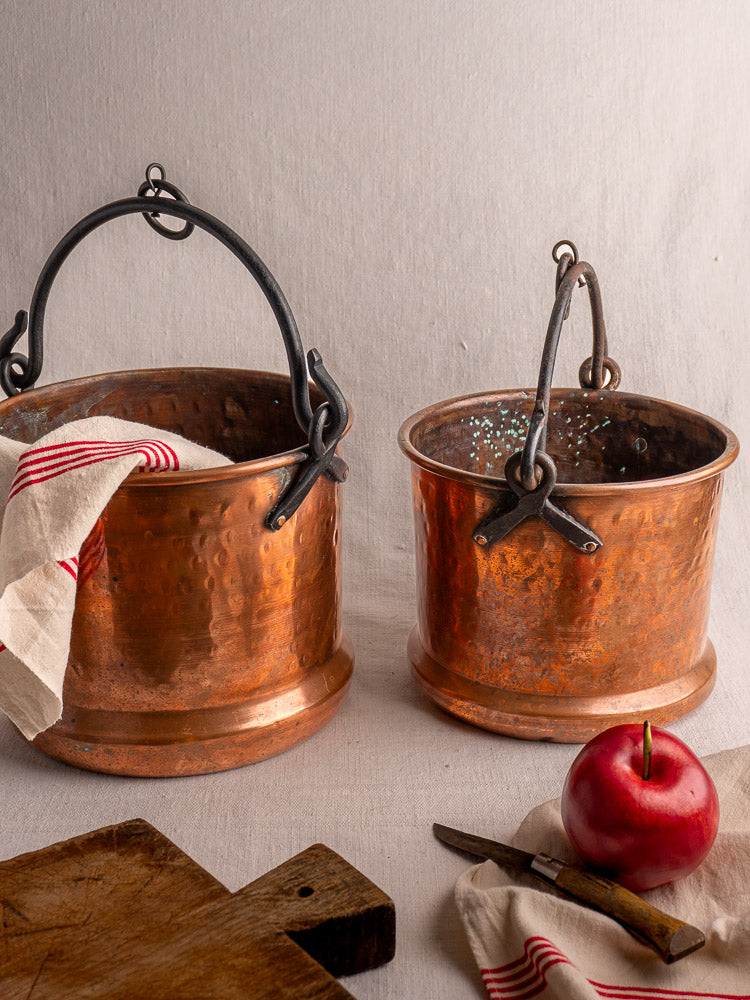 Pair of 19th century French copper hanging buckets with black handles, one holding a striped towel; rustic kitchen accents.