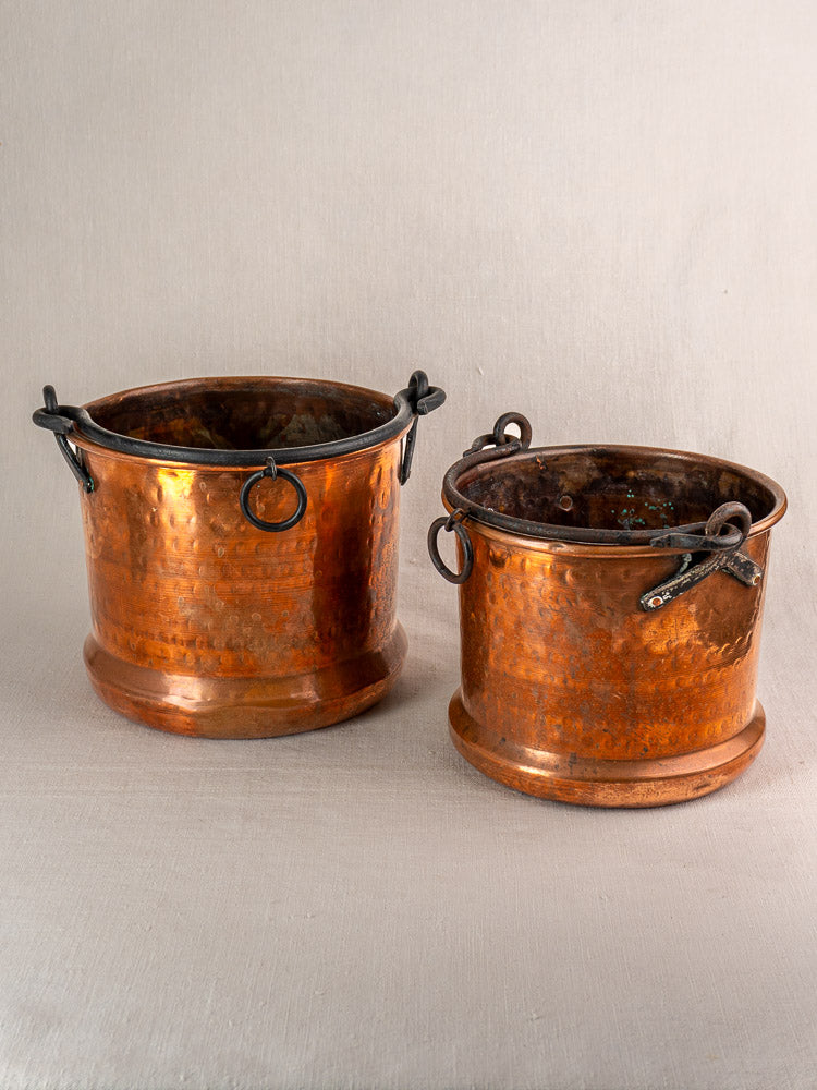 Pair of 19th-century French copper cauldrons with metal handles and rings displayed on neutral fabric.