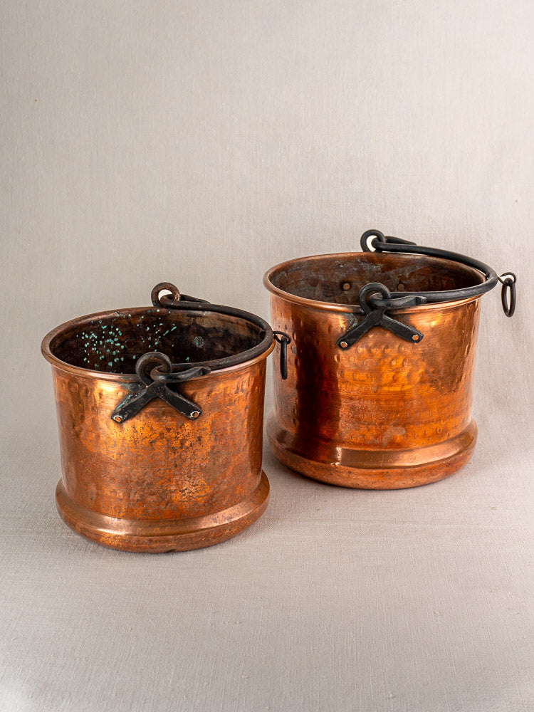 Pair of 19th-century French copper hanging buckets with metal handles and rich patina on neutral fabric.