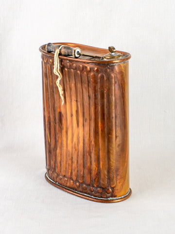 Antique French fluted copper bouillotte hot water bottle with wooden handle on pale background.