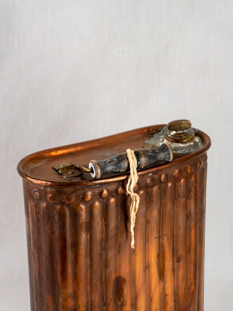 French vintage copper bouillotte with ribbed surface, curved top, and capped spout tied with string.