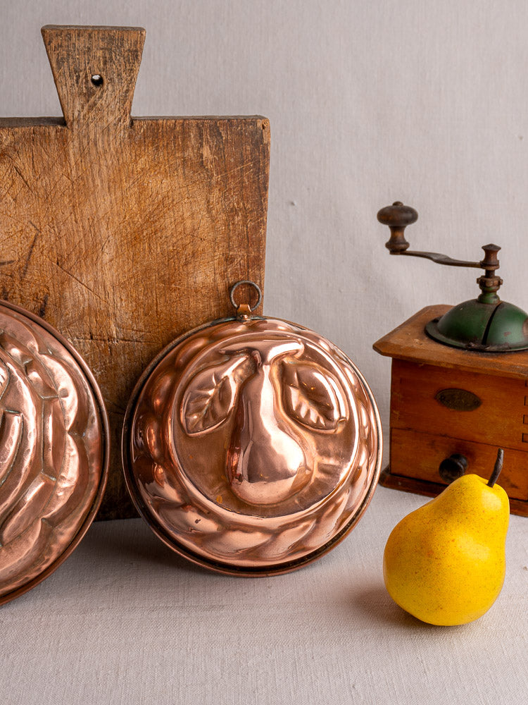 19th-century French copper jelly mold with embossed pear and leaves, decorative border, on a light gray background.