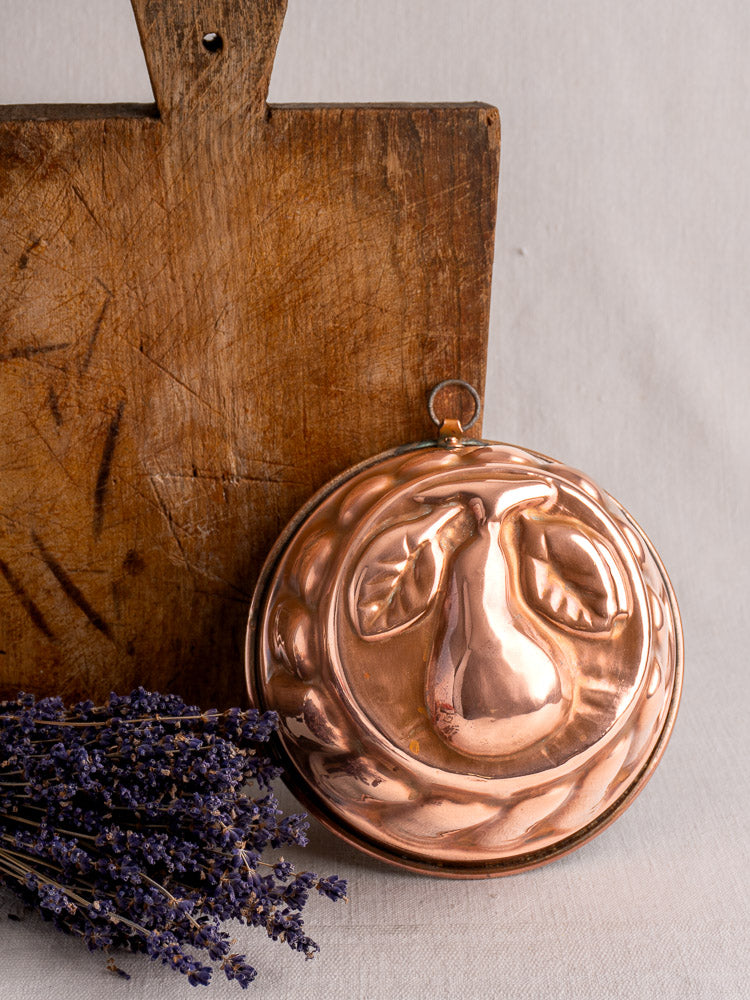 Antique French copper jelly mold with embossed pear motif, set before rustic wood and dried lavender for Provence kitchen appeal.