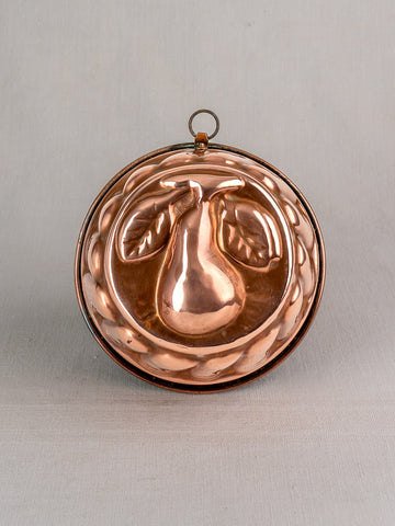 19th-century French copper jelly mold with embossed pear and leaves, decorative border, on a light gray background.