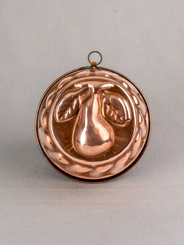 19th-century French copper jelly mold with embossed pear and leaves, decorative border, on a light gray background.