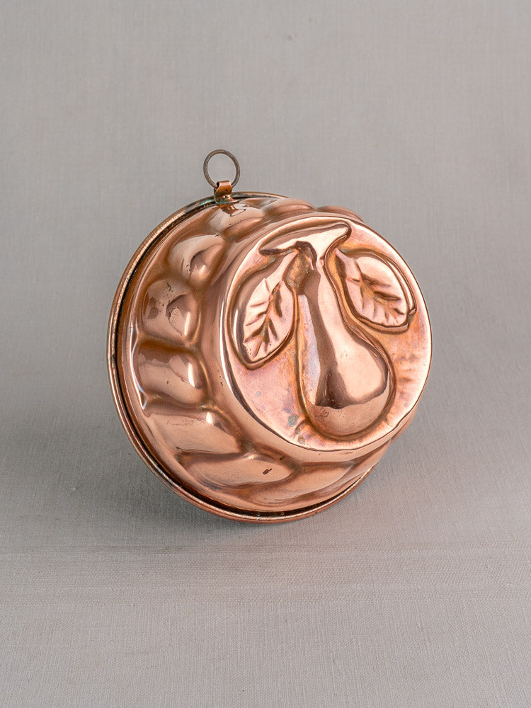 19th-century French copper jelly mold with an embossed pear and leaves, hanging loop for display.