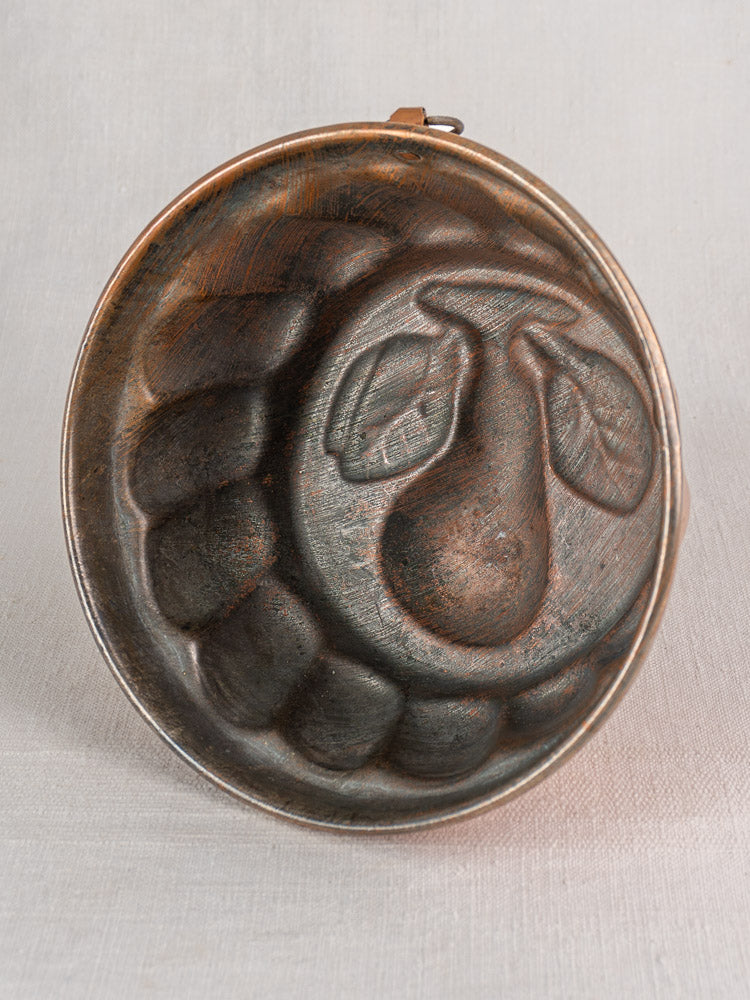 19th-century French copper jelly mold with embossed pear motif and scalloped rim, displayed upright on light fabric.