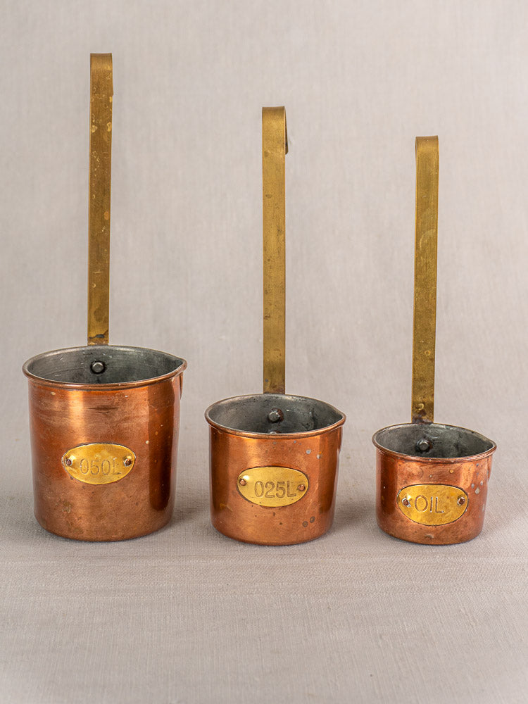 Set of five late 19th-century French copper measuring cups with brass handles and volume labels on a neutral background.