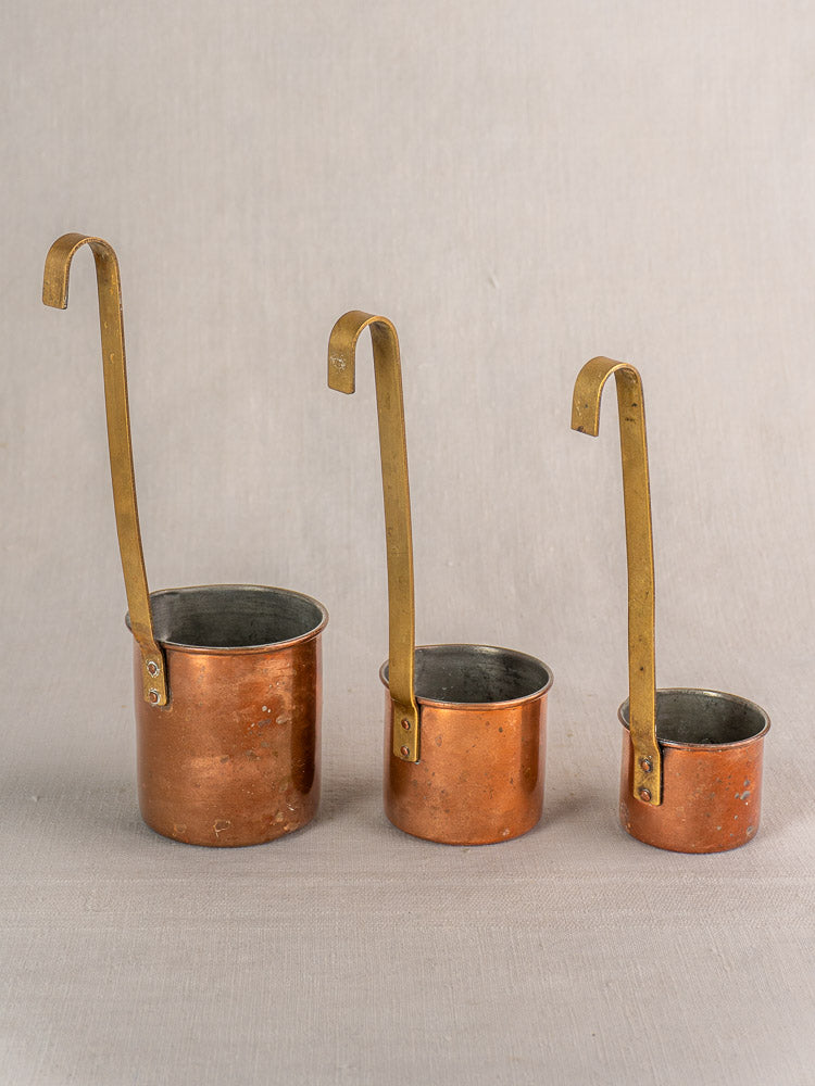 Set of five late 19th-century antique French copper measures with classic design on neutral fabric background.