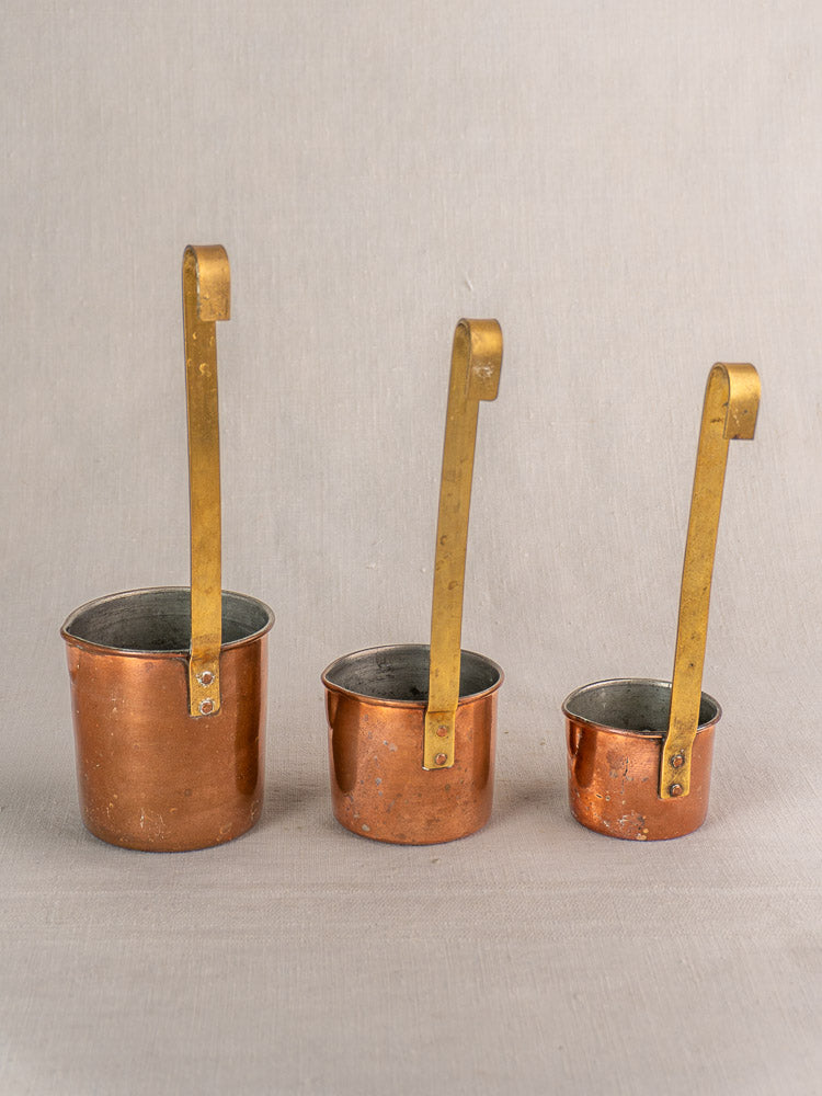 Set of five late 19th-century antique French copper measures with long brass handles, displayed side by side.