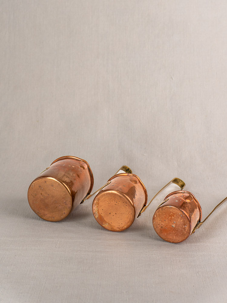 Set of five late 19th-century antique French copper mesures arranged upside down by size on neutral fabric.