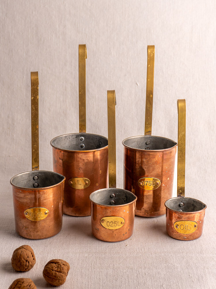 Set of five late 19th-century French copper measures with brass handles and volume labels, grouped with walnuts in front.