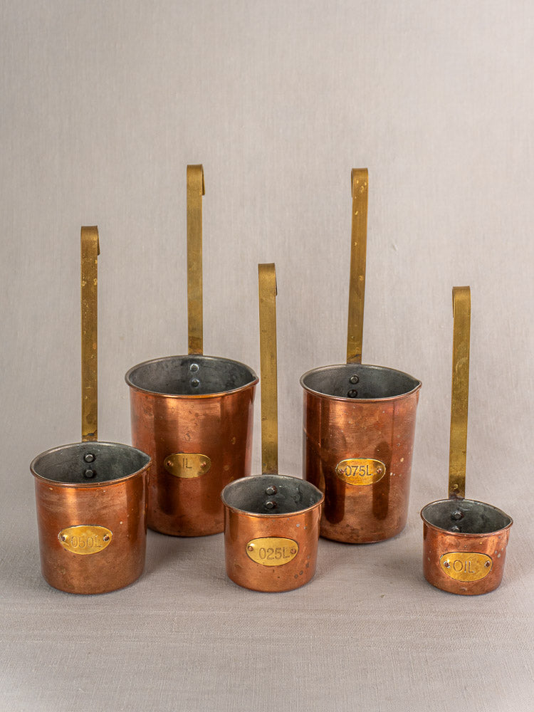 Late 19th century French copper measure set of five, with brass handles and labels, for kitchen decor.