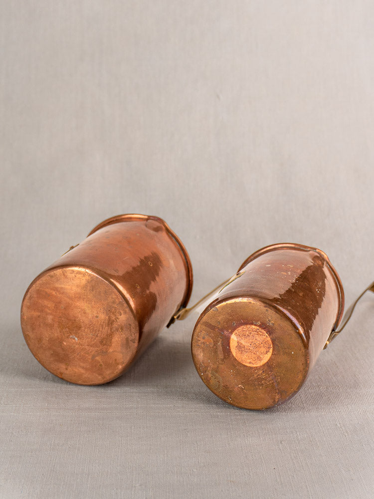 Antique French copper measure set of five with rounded, worn handles on a light gray surface.