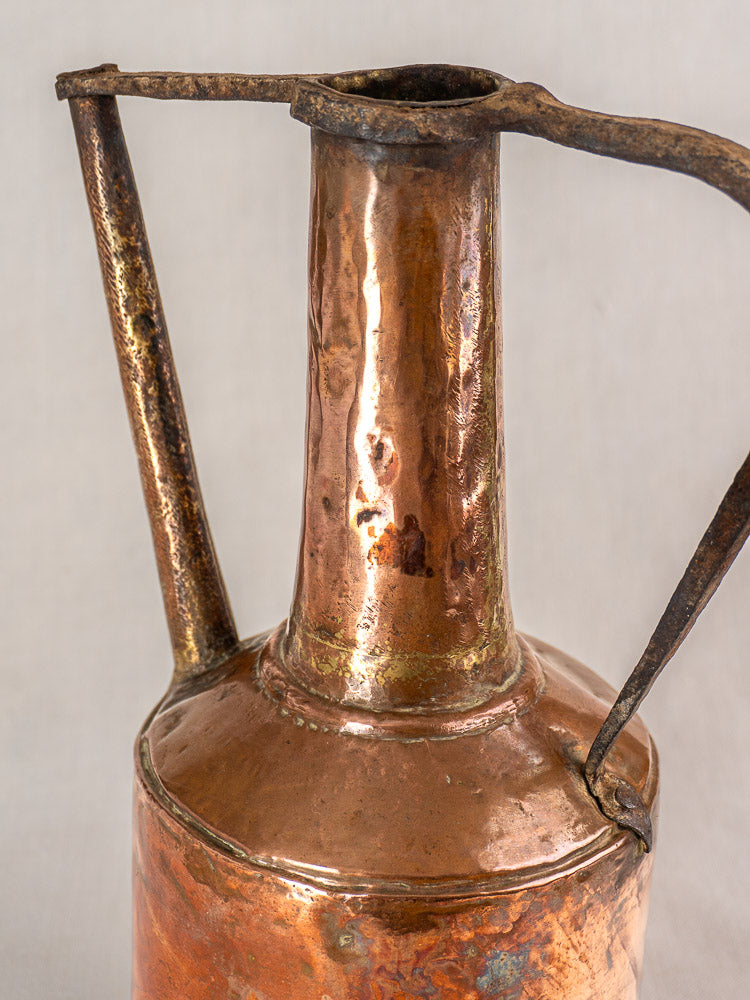 Antique French hammered copper water jar with iron handles and narrow neck, rich patina, on light gray background.
