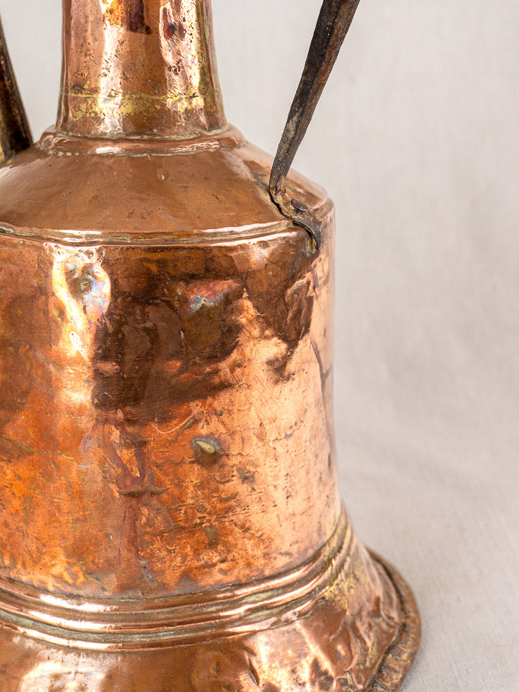 Antique French hammered copper water jar base with twin iron handles, tarnish and wear, on neutral background.