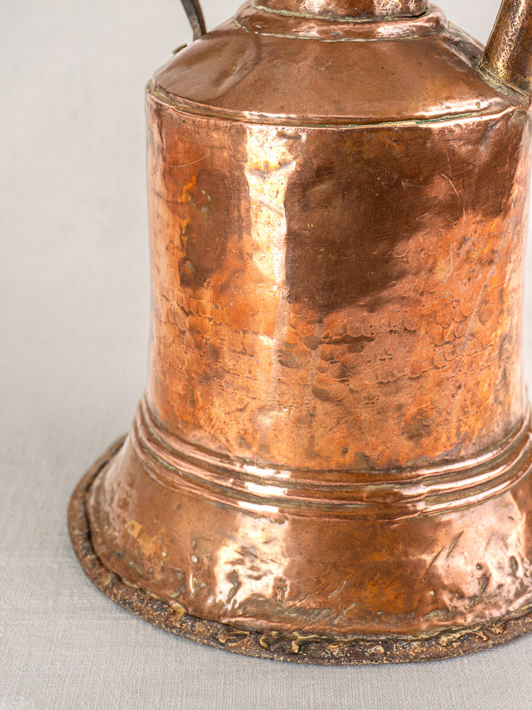 Antique French hammered copper water jar base with twin iron handles, weathered patina on light gray fabric background.