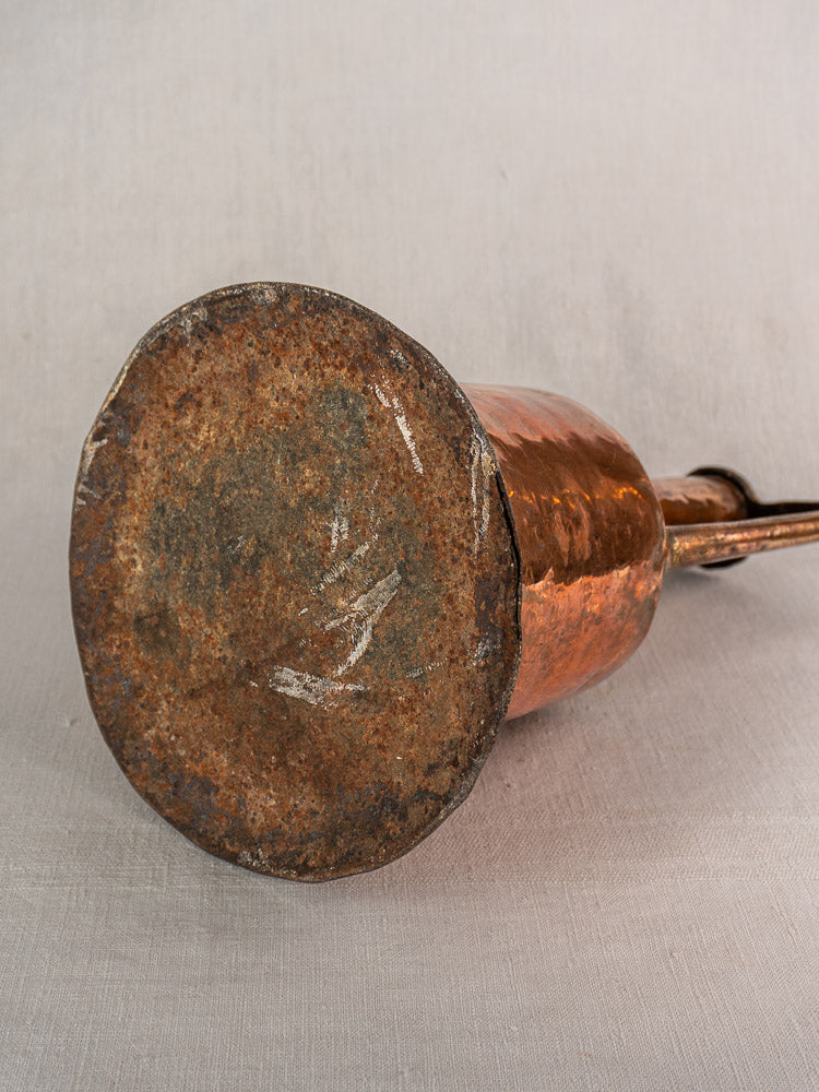 Antique French copper water jar base with hammered finish, twin iron handles, and rusted bottom on neutral fabric.