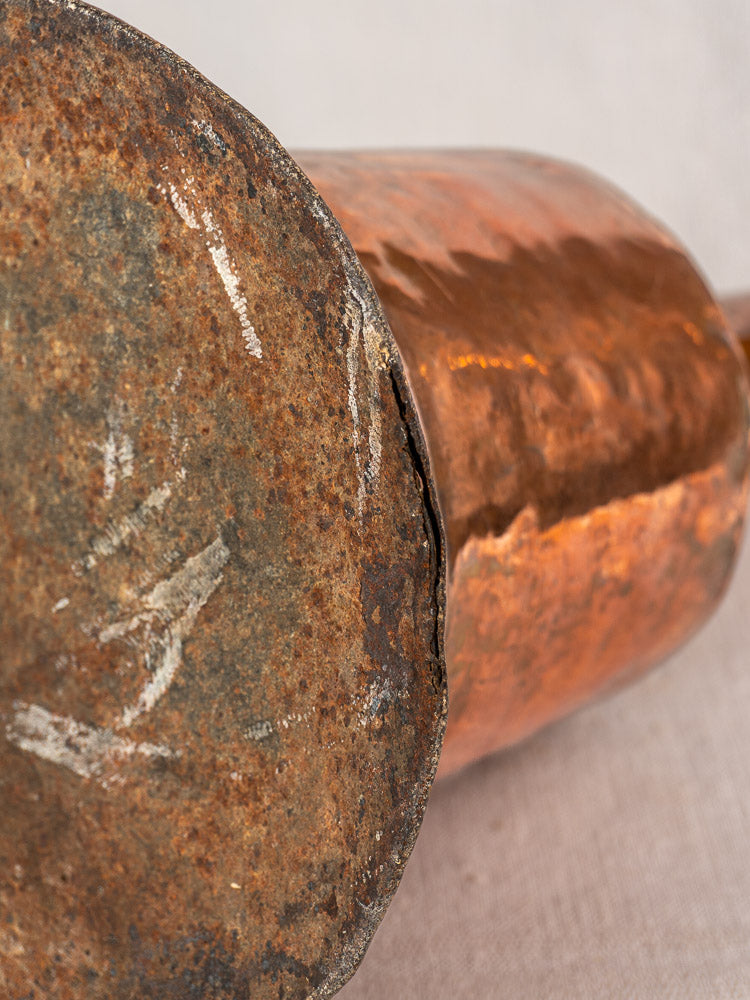 Bottom view of antique French copper water jar, hammered finish, twin iron handles, with tarnish, scratches, and dents.
