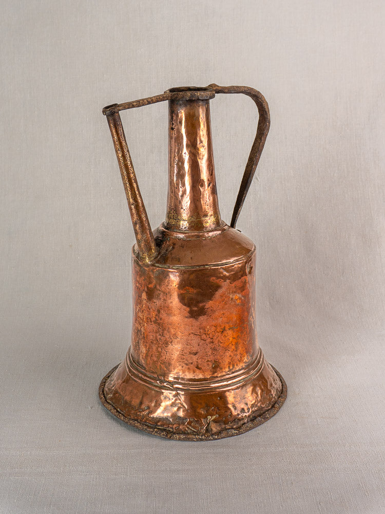 Antique French hammered copper water jar with twin iron handles on neutral fabric background. 19th century.