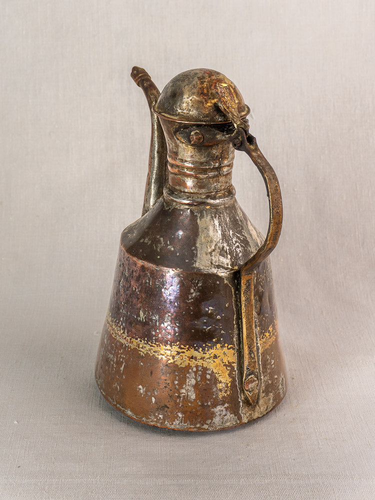 Antique French copper oil pouring jug with rounded lid, curved spout, and sturdy handle on neutral fabric.