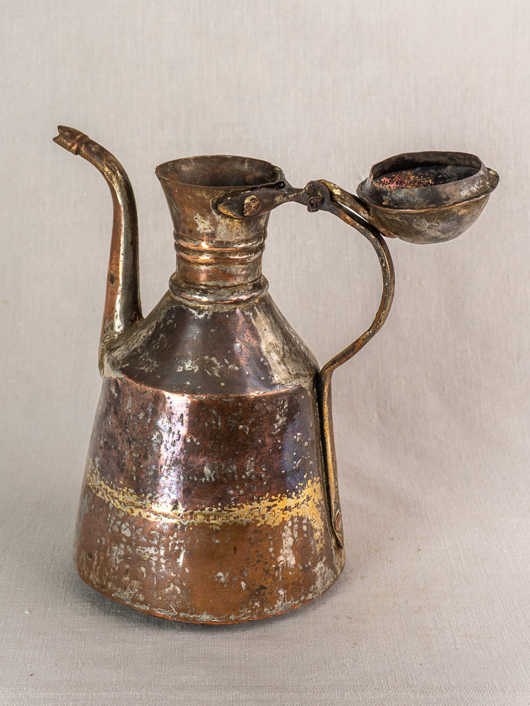 Antique French copper oil pouring jug with long spout, hand hammered, open hinged lid on neutral fabric background.