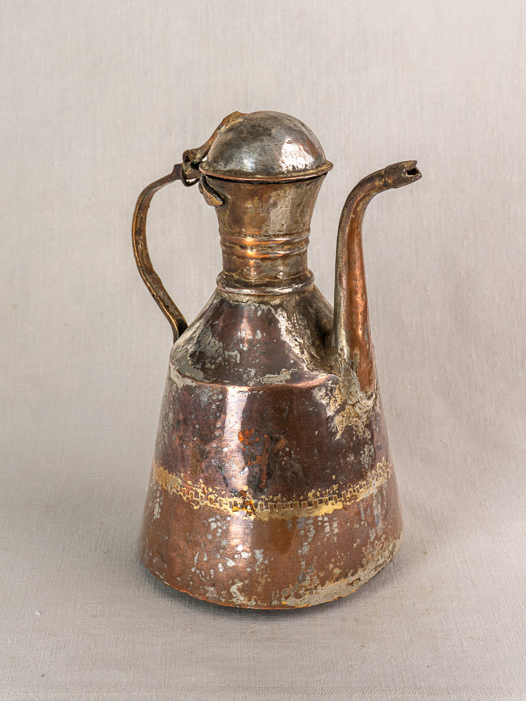 Antique French hand-hammered copper oil jug, 19th century, wear and patina, on neutral fabric background.