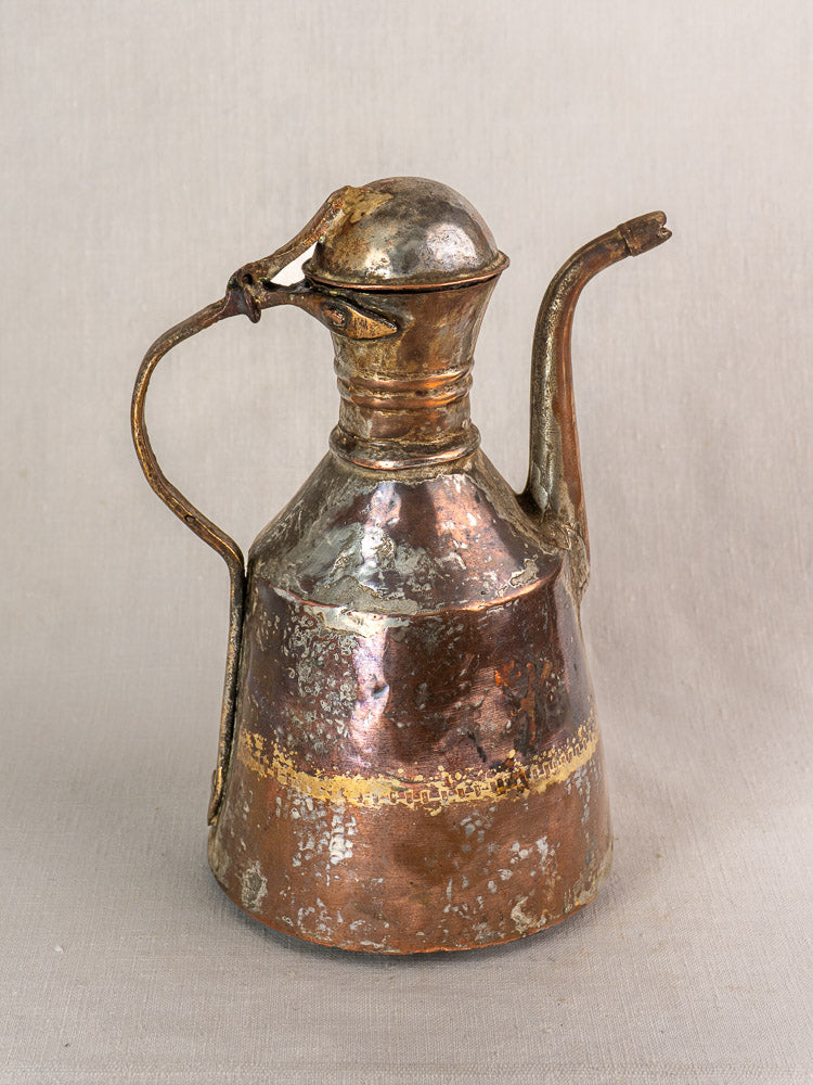 19th-century French antique copper oil pouring jug, hand hammered, with curved spout and rounded lid on neutral surface.