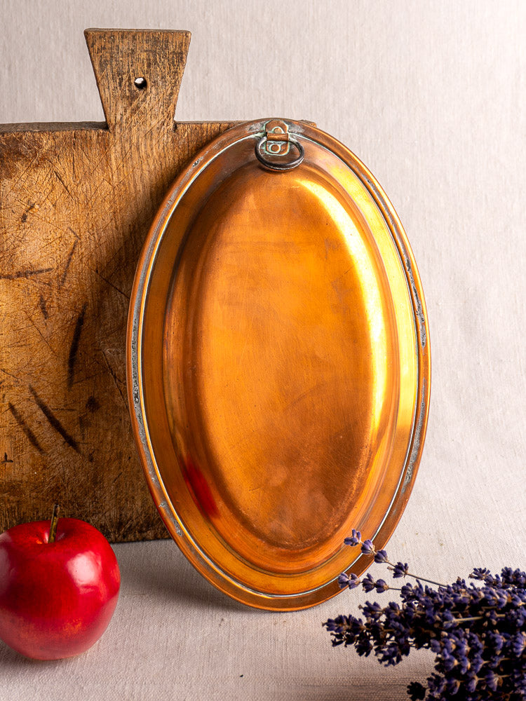 Antique French copper platter with silver trim and hanging ring, styled with red apple and lavender against fabric backdrop.