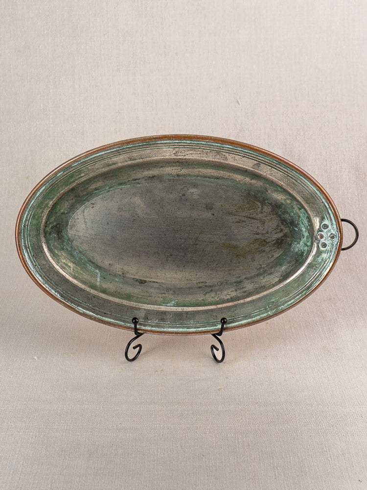 Antique French copper oval platter with tinned interior, greenish patina, hanging ring, raised rim on black metal stand.