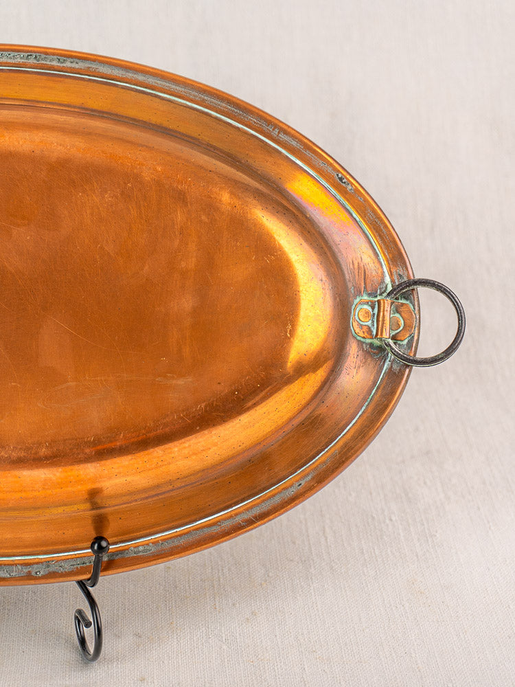 Antique French copper oval platter with tinned interior, hanging ring, warm patina, and edge tarnish on neutral fabric.