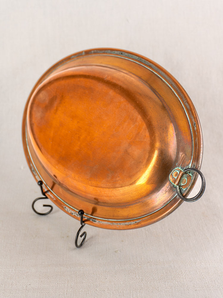 Antique French copper oval platter with tinned interior, raised rim, and hanging ring on black metal display stand.