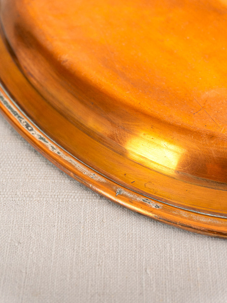 Antique French copper platter with tinned oval design and hanging ring, lightly tarnished rim on beige fabric.