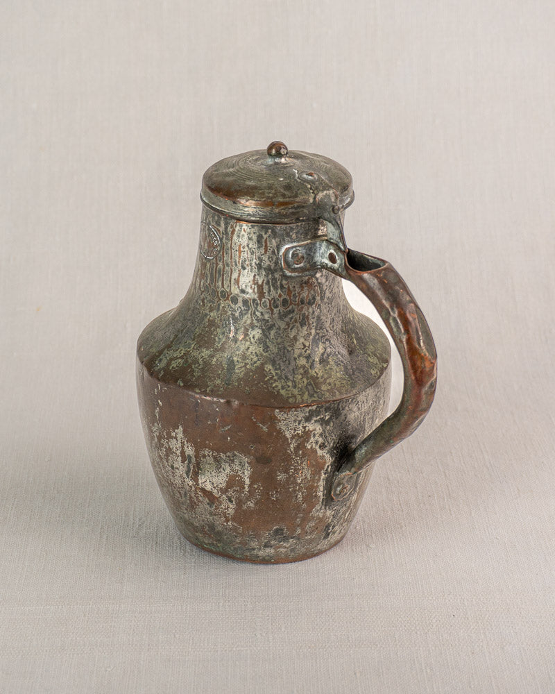 Antique French copper pitcher by Allez Frères Paris with hinged lid, on light fabric background.
