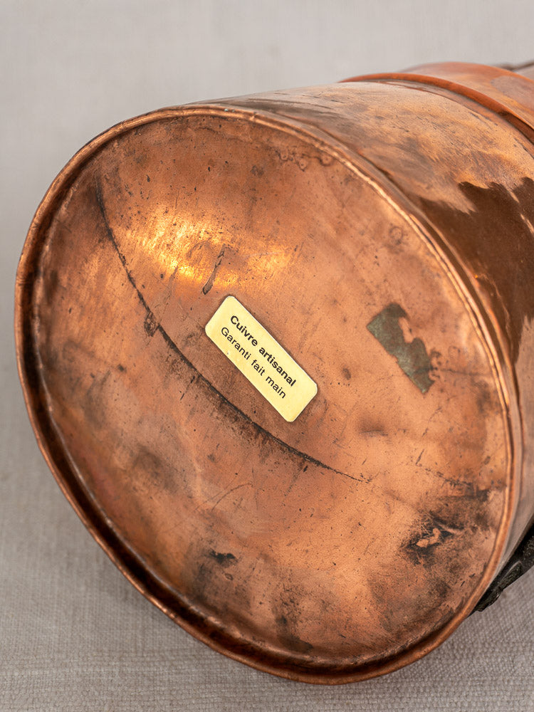 Antique French copper measure jug base, hand-hammered surface, yellow artisan label, and forged iron handle, 19th century.
