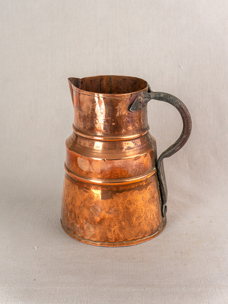 19th-century French antique copper measure jug with hand-hammered finish and forged iron handle on linen background.