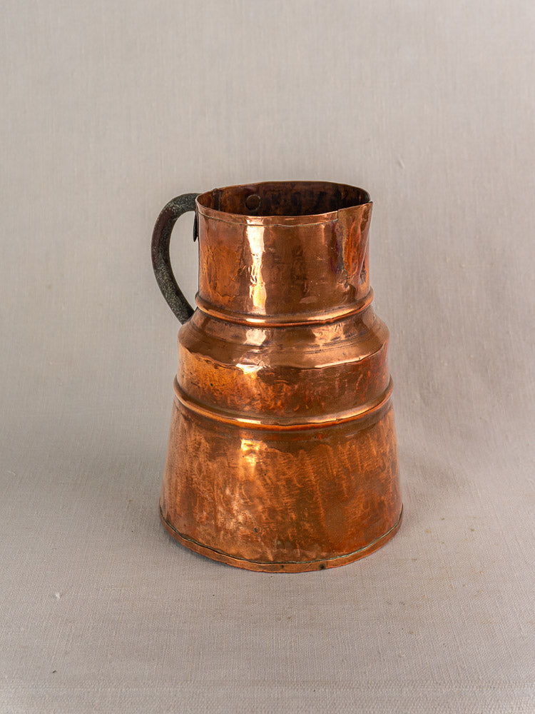 Antique French copper measure jug with forged iron handle on a light gray textured surface, neutral background.