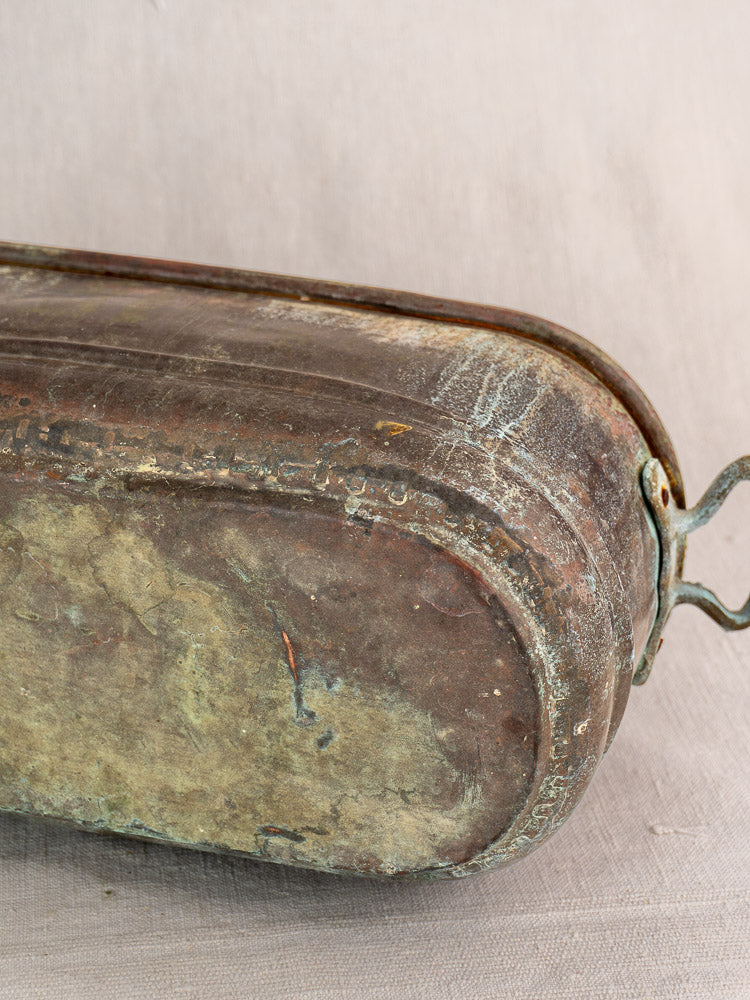 Antique French copper poissonnière jardinière with verdigris patina, aged handle, rust, and oxidation on neutral fabric.