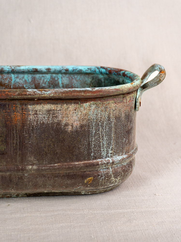 Antique French copper poissonnière jardinière with verdigris patina, rectangular form, looped handle on fabric background.